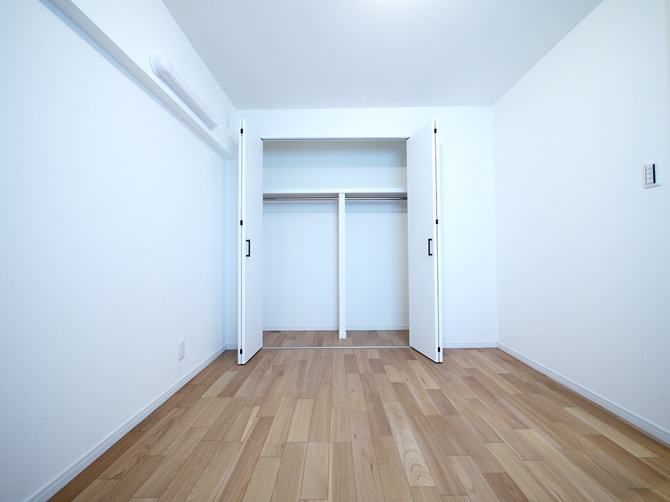洋室の別アングル。フローリングの質感と壁紙が明るい室内を演出している。