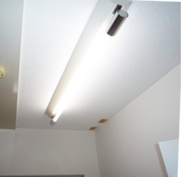 修復後の状態。左側の古い蛍光灯が撤去され、モダンなLED照明器具に交換されている。照明は明るく点灯し、天井クロスも新しい白く美しいものに張り替えられ、部屋全体が清潔で明るい雰囲気に一新されている。