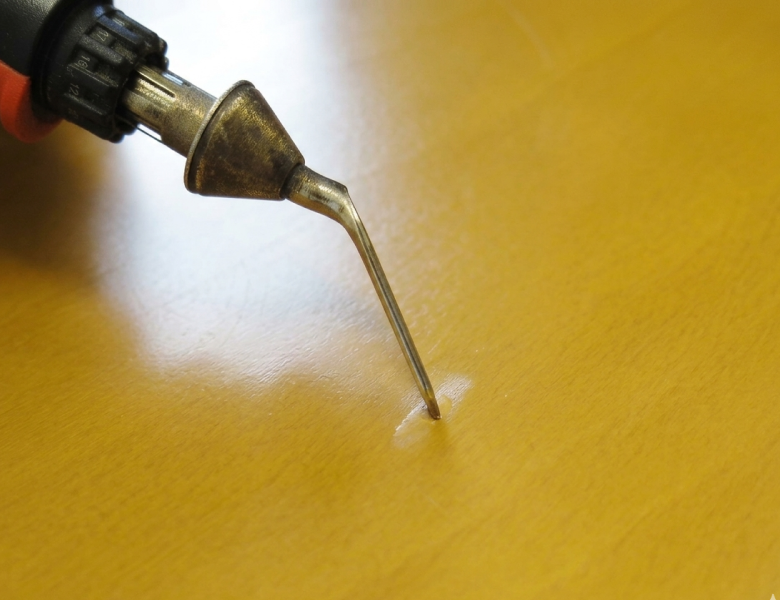 色を合わせた木質用パテをテーブルの凹んだ傷口にしっかりと埋めて充填している作業風景
